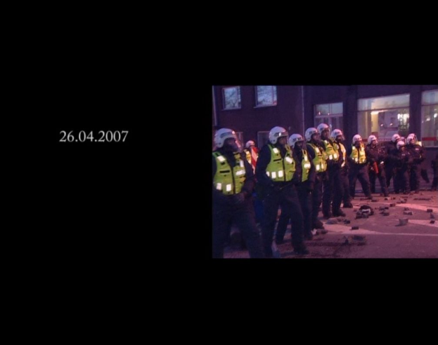 Gruppe von Polizeibeamten in Helmen und Jacken vor einem Gebäude mit Fenstern, mit einem Datum auf der linken Seite.