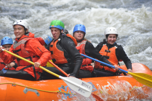Eine Gruppe von Menschen mit Paddeln sitzt in einem aufblasbaren Boot auf dem Wasser.