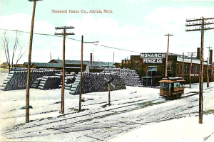 Eine schneebedeckte Landschaft mit einem Fahrzeug auf einer Spur, umgeben von Pfählen, mit einer Sammlung von Gegenständen hinter den Pfählen und einem Fabrikgebäude im Vordergrund.