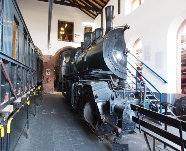 Alte Dampflokomotive wird in einem Museum von innen gezeigt, umgeben von Informationsschildern, Geländern und Beleuchtung.