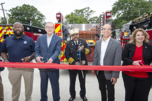 Eine Gruppe von Menschen schneidet ein rotes Band vor einem Feuerwehrauto durch, feiernd die Einweihung der Alexandria Fire Department.