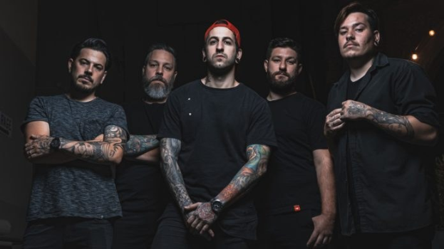 Eine Gruppe von Männern, die in einem dunklen Raum mit Licht auf der rechten Seite stehen und scheinbar ein Interview für Avenged Sevenfold geben.