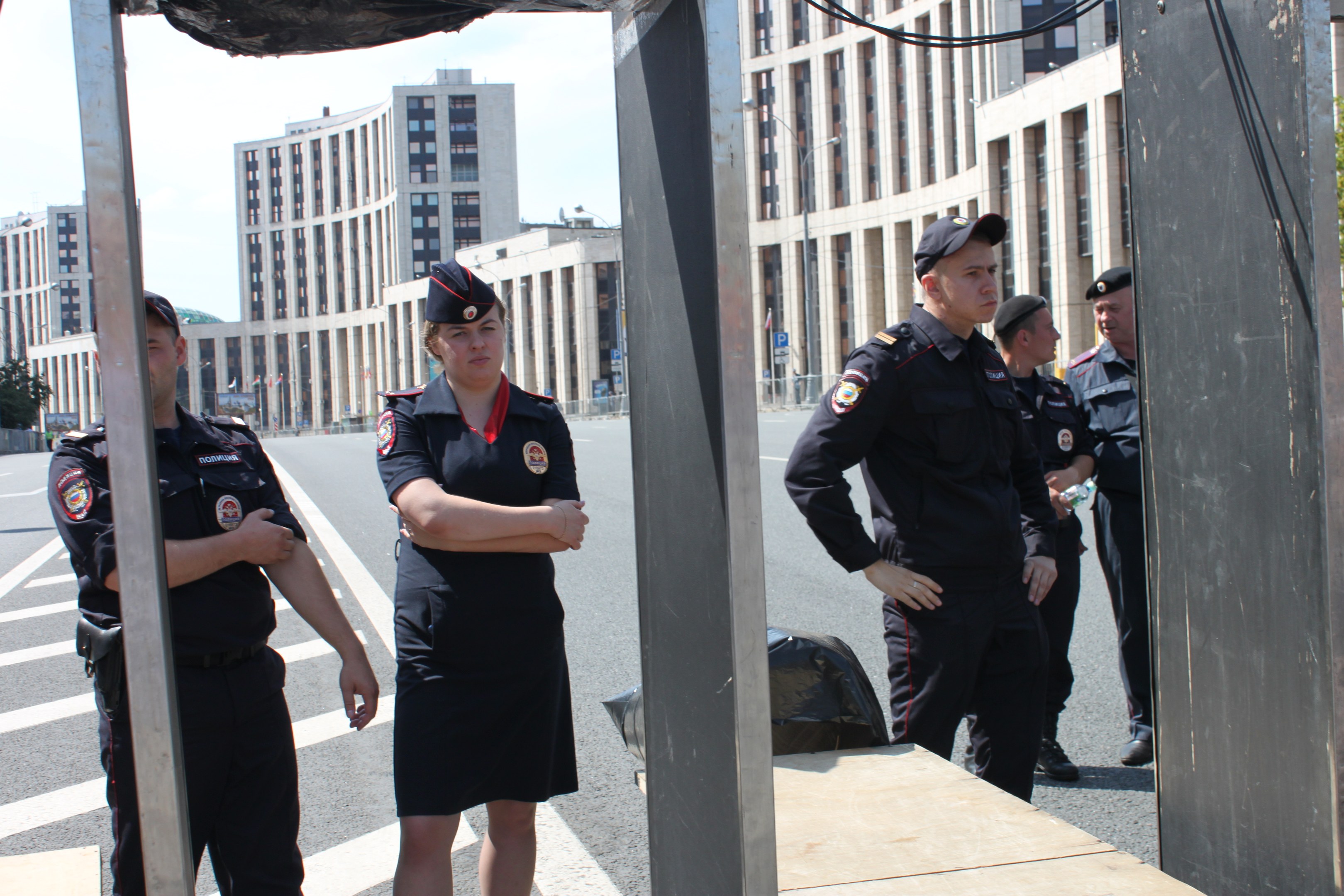 Gruppe von Polizisten in Uniform auf einer Straße mit Polen und Drähten im Vordergrund, Gebäuden, Bäumen und einem klaren blauen Himmel im Hintergrund.