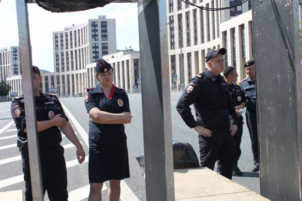 Gruppe von Polizisten in Uniform auf einer Straße mit Polen und Drähten im Vordergrund, Gebäuden, Bäumen und einem klaren blauen Himmel im Hintergrund.