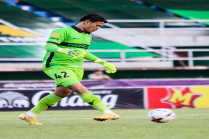Ein Mann in einem grünen Torwarttrikot schießt einen Fußball auf einem Rasenfeld in einem Stadion, im Hintergrund sind Banner mit "Chivas USA gegen Mexico City, 3-1, Copa Libertadores" zu sehen.