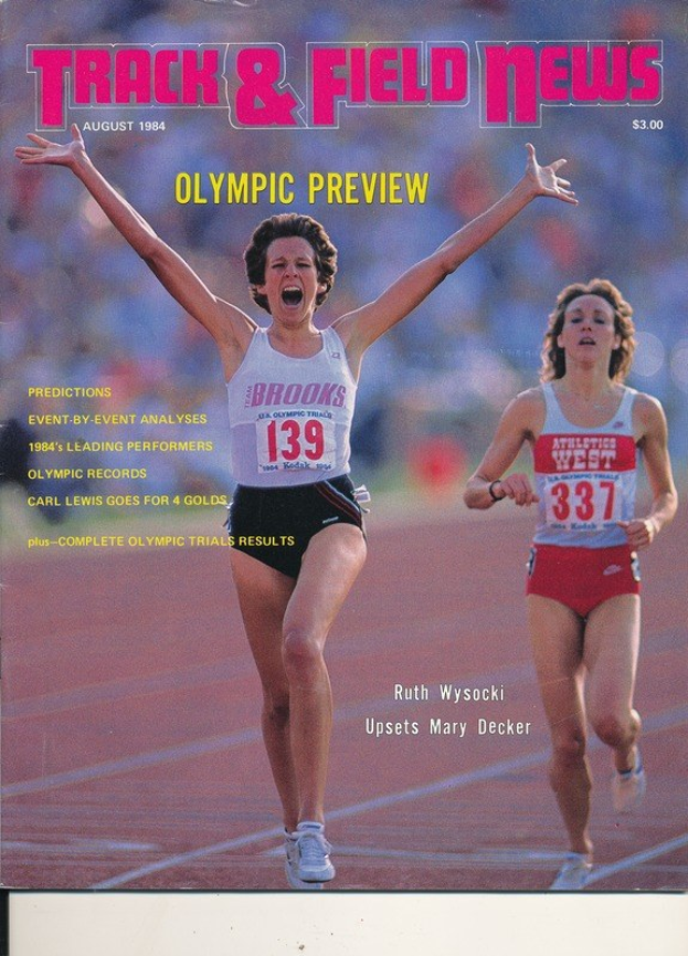 Zwei Frauen in Laufkleidung sprinten auf einer grünen Bahn unter einem blauen Himmel, mit "Track & Field News" auf dem Cover des Magazins.
