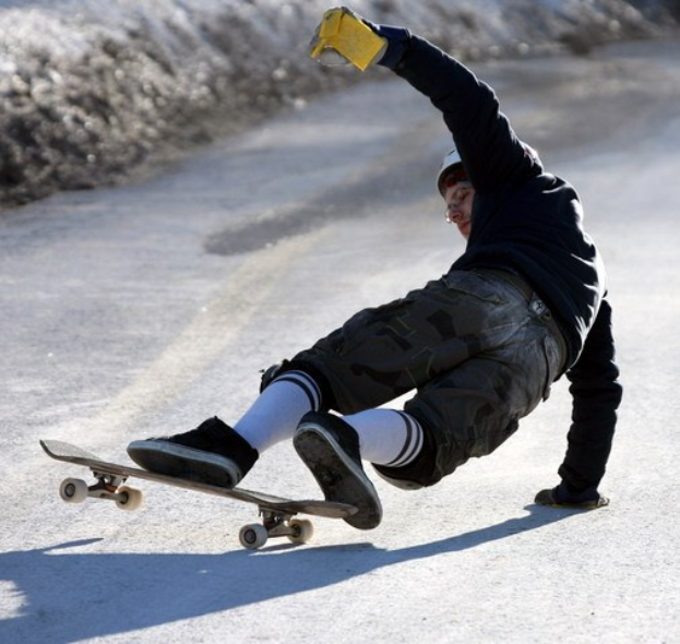 Ein Skateboarder führt einen Sprungtrick auf einer Straße aus, umgeben von sonnenbeschienenen Pflanzen, wobei das Skateboard und die ausgestreckten Gliedmaßen des Fahrers sichtbar sind.